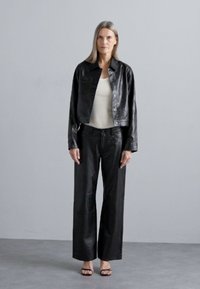 Black leather cropped jacket over white tank top, paired with black leather wide-leg pants. Smooth texture with minimal detailing, featuring no visible hardware.