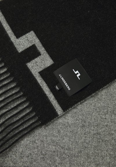 Écharpe à motif noir et gris avec des franges, présentant un design géométrique et une étiquette de marque portant "J. Lindeberg" en blanc.