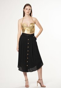 Top bustier metálico dorado con diseño acanalado, combinado con una falda negra de cintura alta que presenta botones de madera y una cintura ceñida con cinturón.
