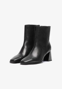 Sorte lær ankelsko med spiss tå, glidel�ås på siden og en chunky geometrisk hæl. Glatt tekstur med minimalistisk design.