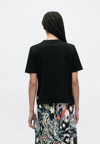 Zwart T-shirt met korte mouwen en een ronde hals. De stof lijkt glad. Onderaan de rug is een klein logo zichtbaar.