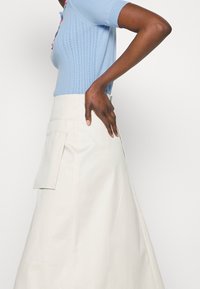 Light blue knit top with short sleeves and textured ribbing, paired with a cream A-line skirt featuring a side pocket detail.
