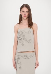 Graues Leinen-Crop-Top mit dünnen Trägern, das mit strukturierten, floralen Applikationen auf der Vorderseite verziert ist. Das Design wird durch einen passenden Rock ergänzt.