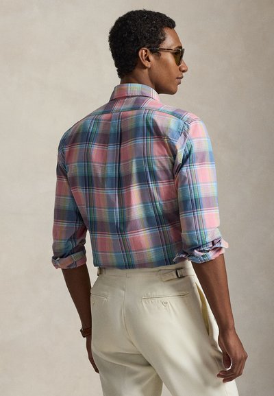 Multicolored plaid shirt featuring a button-down collar, rolled sleeves, and a lightweight fabric, paired with cream-colored trousers.