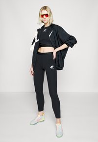 Črna Nike jakna in kratka majica, črne legice z logotipom ter večbarvni športni čevlji z odsevnimi poudarki in elegatnim dizajnom.