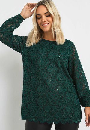 Long-sleeve top in dark green lace with floral pattern and sequins. Features a scalloped hem and a loose fit. Smooth texture, lightweight design.