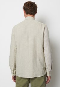 Helles beiges Langarmhemd aus Leinenstoff. Es hat eine schlichte Webart, einen Kragen und Knopfmanschetten sowie einen leicht abgerundeten Saum.