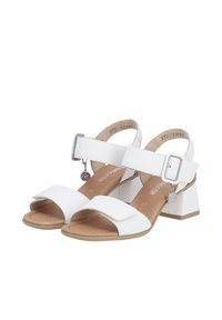 White sandals with a block heel, open toe, and ankle strap. Features large buckle and charm detail. Soft textured insole.