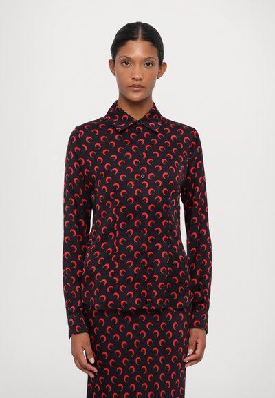 Blusa nera con motivo a mezzaluna rossa, maniche lunghe e colletto. Presenta una chiusura frontale con bottoni e una texture di tessuto liscia.