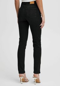 Vaqueros skinny de mezclilla negra con bolsillos traseros, cintura alta, acentos de costura mínimos y una etiqueta de marca de cuero marrón en la parte de atrás.