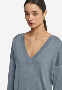 Szary, dzianinowy pulower z głębokim dekoltem w kształcie V, długimi rękawami oraz prążkowanymi akcentami przy dekolcie i na dole. Gładka faktura.