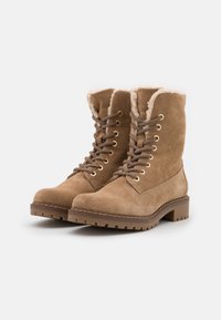 Botas de ante marrón con cordones, con un cuello de piel acolchado, ojales metálicos y una suela de goma texturizada. Diseñadas para la durabilidad y el calor.