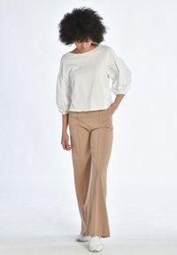 Vit kort topp med puffärmar, kombinerad med högmidjade beige byxor som har sömnadsdetaljer och utsvängda ben.