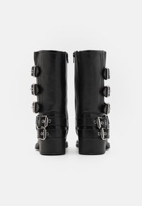 Svarta knähöga läderstövlar med silverfärgade metalldetaljer, flera spännen och sidostängning med dragkedja, rejäla klackar.