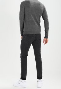 Pull gris, jeans noirs et baskets blanches. Les jeans sont ajustés avec une légère élasticité, et le pull a un motif de tricot texturé.