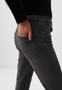 Jeans en denim gris au design ajusté, avec une poche arrière et des détails de couture subtils. Le tissu semble légèrement texturé.