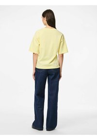 T-shirt en coton jaune à coupe décontractée et manches courtes, associée à un jean en denim sombre à jambes larges. Design simple, sans motifs ni accents visibles.