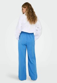 Chemise blanche à boutons avec manches longues et coupe décontractée, associée à un pantalon bleu à jambes larges avec une ceinture élastique.