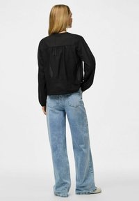 Svart, långärmad, lätt blus med en samlad detalj på ryggen, tillsammans med högmidjade, urblekta blå vida jeans och bruna sneakers.