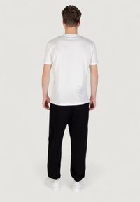 Witte T-shirt met korte mouwen en zwarte broek gedragen door een persoon, met een eenvoudig ontwerp en een relaxte pasvorm. Effen stof, geen zichtbare patronen.