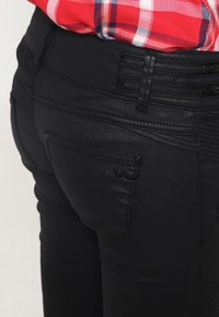 Svarta denimjeans med texturerade detaljer, blixtlås och design med flera fickor. Ajusterad passform med tonade sömmar. Lämpliga för avslappnad klädsel.