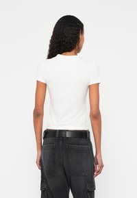 Balta īsroku T-krekls ar apaļu apkakli, kopā ar tumši pelēkām džinsa kravas biksēm ar lielām kabatām un melnu jostu.