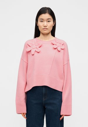 Rožinis trumpintas megztinis su ilgomis rankovėmis, ant pečių puoštas gėlių aplikacijomis, su ribojimu apykaklėje ir apačioje. Derinkite su tamsiai mėlynais džinsais.