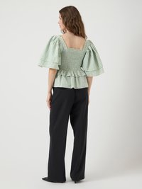 Blusa verde a quadretti con maniche a palloncino e busto arricciato. Presenta un orlo arricciato e un retro quadrato, abbinata a pantaloni neri a gamba larga.