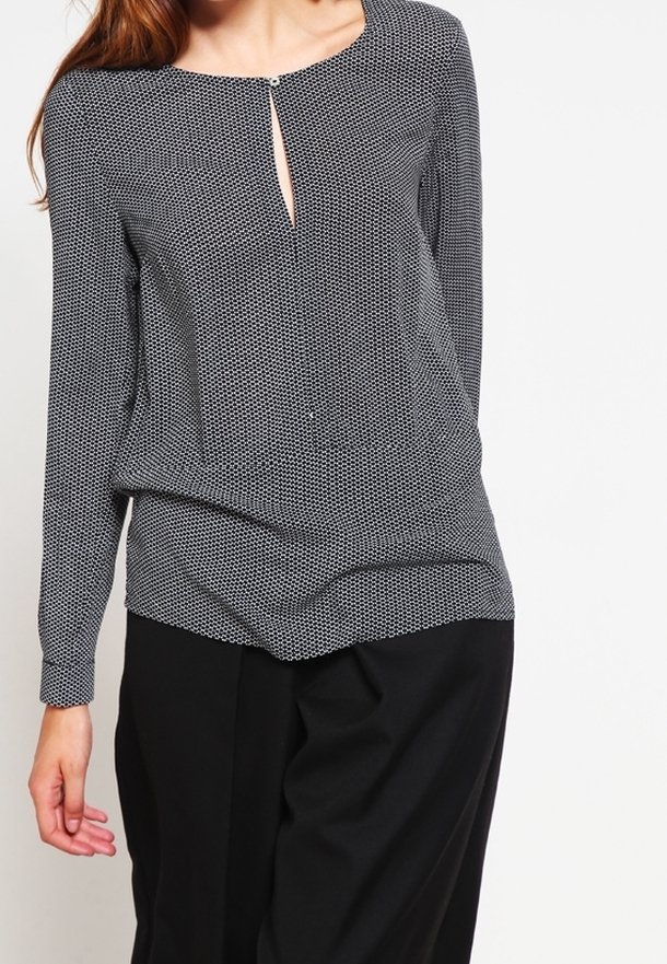 Femme portant un chemisier à manches longues noir et blanc avec un petit décolleté en trou de serrure et un pantalon noir ample.