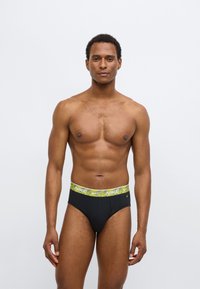 Černé slipy s neonově žlutým, texturovaným pasem s logem Nike. Hladká, pružná látka a klasický střih. Bez dalších vzorů.