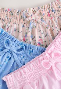 Cinturas elásticas con lazos de tela en tres pares de pantalones cortos infantiles en rosa, azul con flores y rayas rosas con flores.