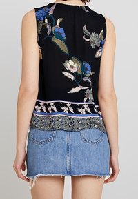 Haut sans manches noir avec broderie florale en bleu et vert, doté d'un ourlet inférieur à motifs et associé à une mini-jupe en denim effilochée.