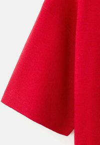 Red fabric with visible stitching, showing a close-up of the sleeve hem of a knitted garment against a white background.