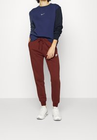 Marinblå och svart färgblockerad sweatshirt med en liten grå Nike-logga, i kombination med burgundy joggers som har en vit Nike-logga. Vita sneakers.
