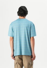Lys blå kortermet t-skjorte med horisontale striper, rund hals, mykt stoff, avslappet passform. Brukt med beige cargo-bukser.
