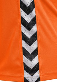 Orange atletisk tröja med ett texturerat svart och vitt chevronmönster längs sidan, med en slät tygfinish.