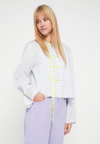 Langærmet, kort skjorte i lyst ternet mønster med gule accenter. Fremstillet af let vævet stof. Sat sammen med lilla fløjlsbukser.