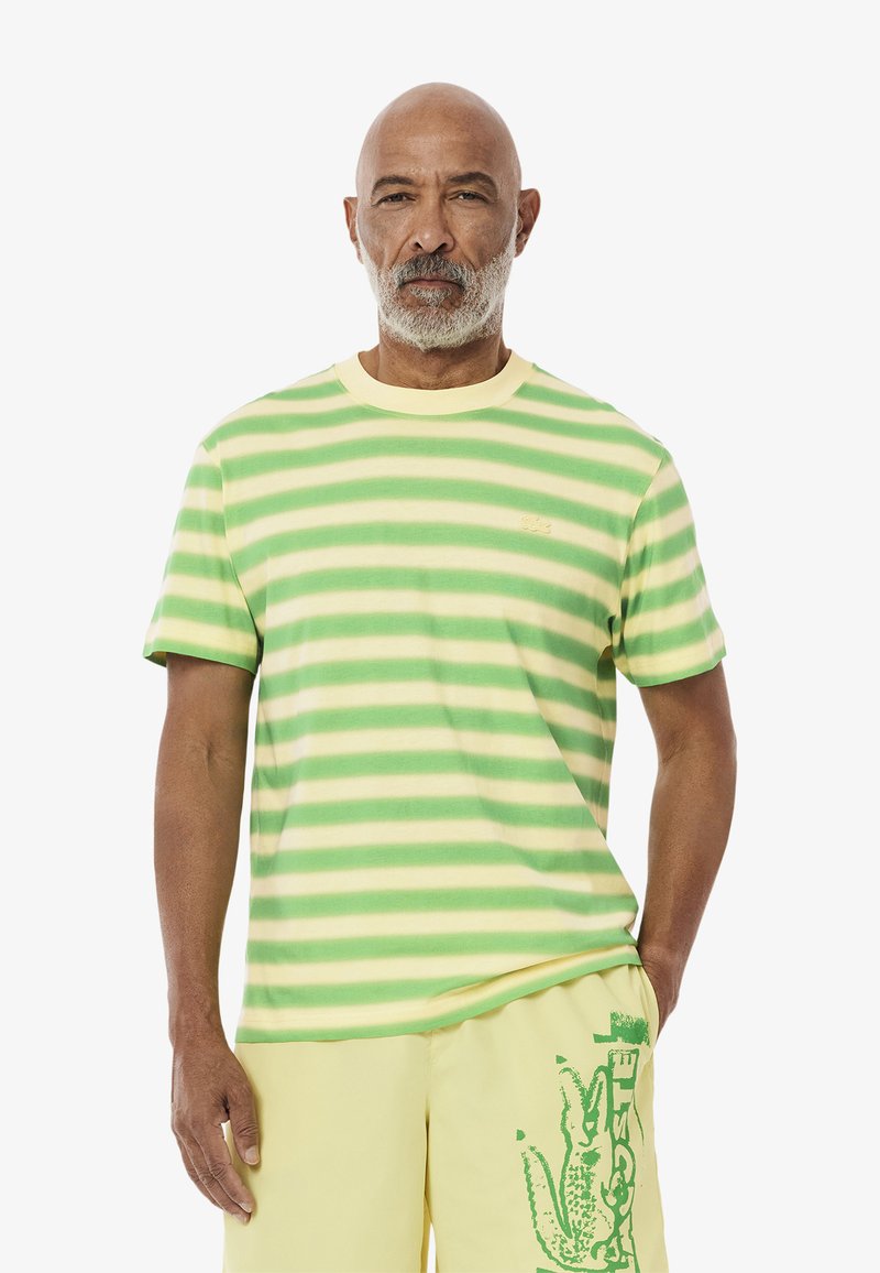 T-shirt a righe nei colori verde e giallo, con scollatura a girocollo, maniche corte e un piccolo logo sul lato sinistro del petto. Materiale in cotone.