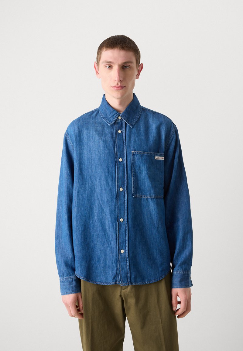 Jeanshemd in Mittelblau mit langen Ärmeln, einem Kragen und einer Brusttasche. Mit weißen Knöpfen und einem dezenten Markenlabel.