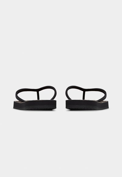 Μαύρα επίπεδα σανδάλια με λεπτές λουρίδες, εμφανιζόμενα από πίσω σε απλό ανοιχτό φόντο.