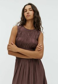 Klänning i en mörk mauve färg med en åtsittande bodice, samlad textur och utsvängd kjol, med rund halsringning och ärmlös design.