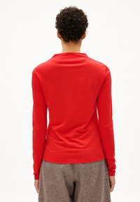 Rotes Langarmshirt mit rundem Halsausschnitt und eng anliegenden Ärmeln, kombiniert mit grauen strukturierten Hosen. Glatter Stoff, schlichtes Design.