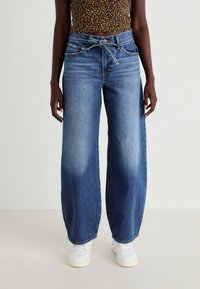 Vaaleat siniset leveälahkeiset farkut haalistuneella pinnalla, joissa on naru vyötäröllä, kaksi etutaskua ja näkyvät ompeluyksityiskohdat.