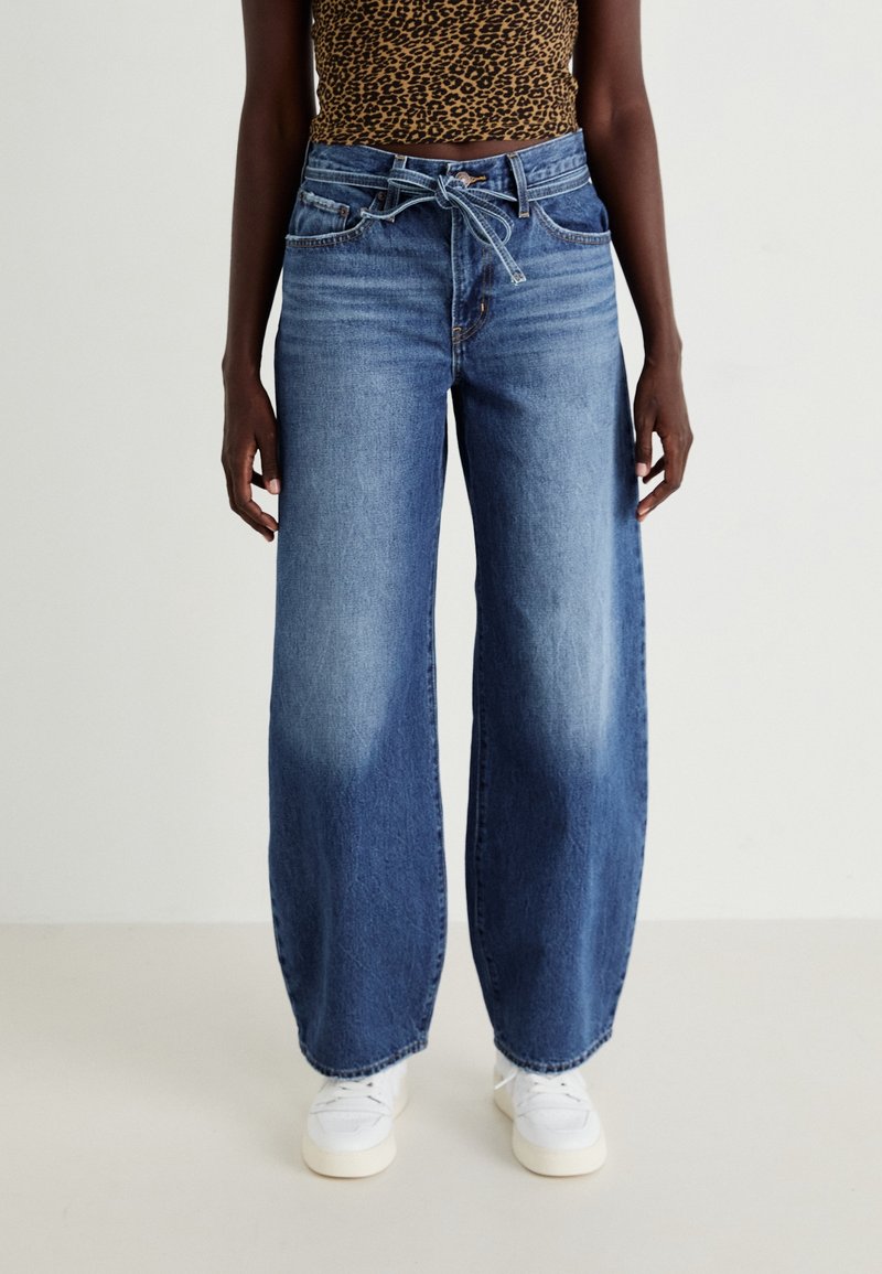 Vaaleat siniset leveälahkeiset farkut haalistuneella pinnalla, joissa on naru vyötäröllä, kaksi etutaskua ja näkyvät ompeluyksityiskohdat.