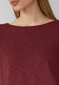 Burgunderfarbener, locker sitzender Oberteil mit weitem Ausschnitt, aus einem weichen, strukturierten Stoff und subtiler Melierung. Glatte Verarbeitung, lässiges Design.
