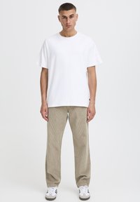 White cotton t-shirt with a relaxed fit paired with beige corduroy pants. Shoes are white with gray and black accents.