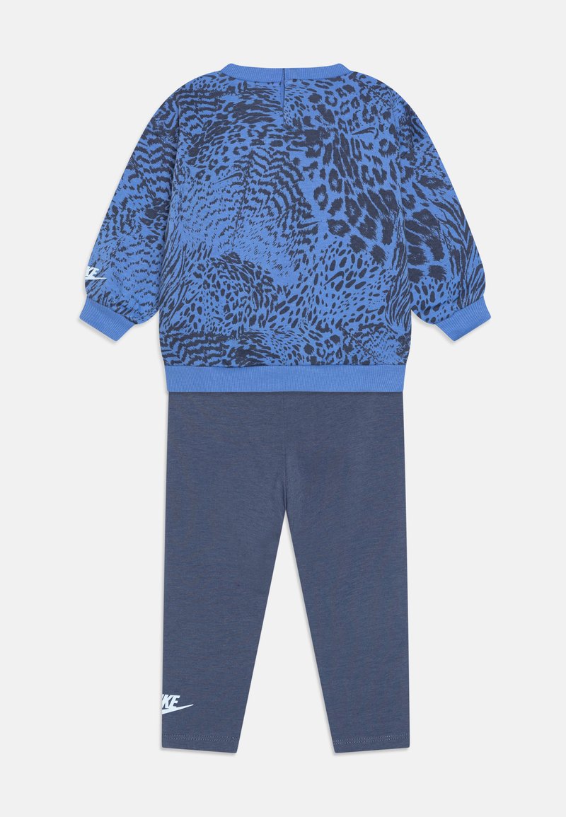 Sweat-shirt bleu avec un imprimé animal texturé, associé à des leggings bleu marine unis. Détails de logo blanc sur les leggings. Tissu doux, coupe décontractée.