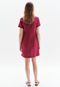 Vestito fucsia a maniche corte con taglio dritto, texture liscia e dettagli delle cuciture; abbinato a sandali marrone chiaro.