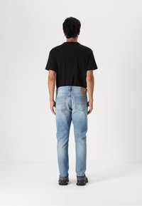 Un tricou scurt negru cu mânecă scurtă purtat cu blugi de culoare bleu deschis. Blugii au o croială dreaptă clasică, câteva estompari subtile și buzunare la spate.