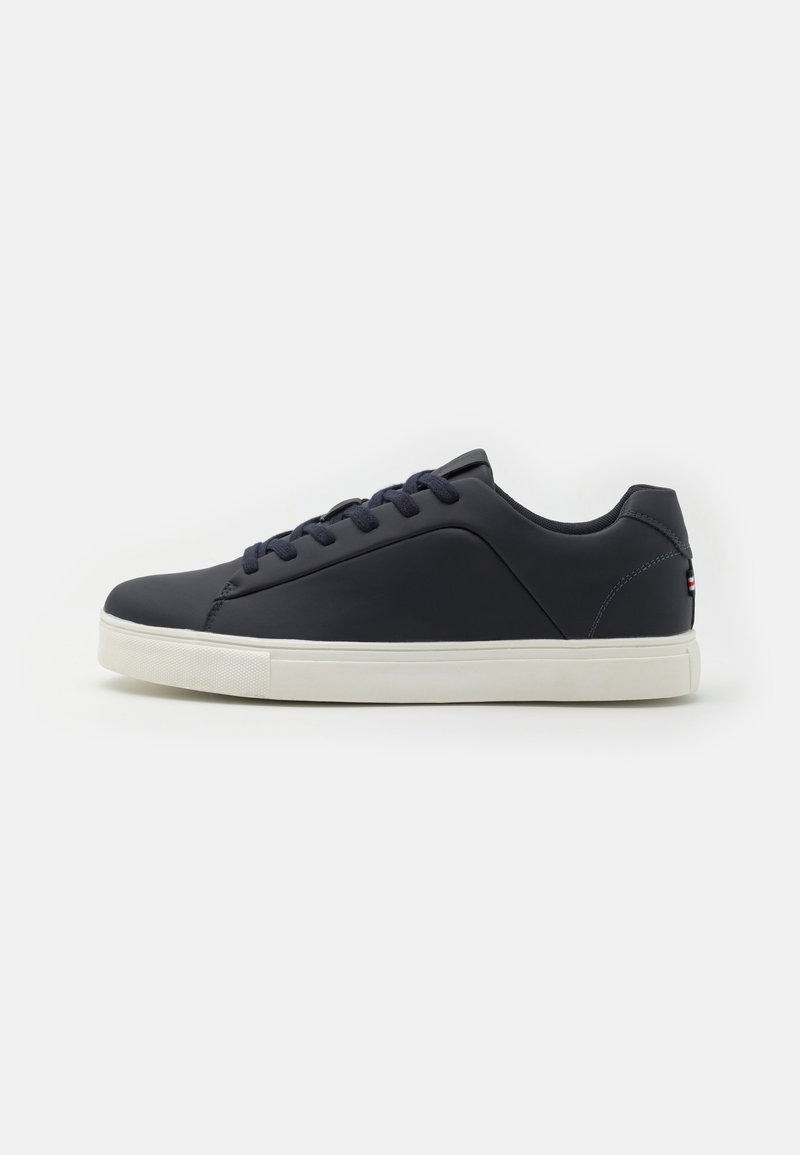 Navy blue sneaker with a smooth synthetic upper, round toe, white rubber sole, and navy laces. Features a subtle logo detail on the heel.